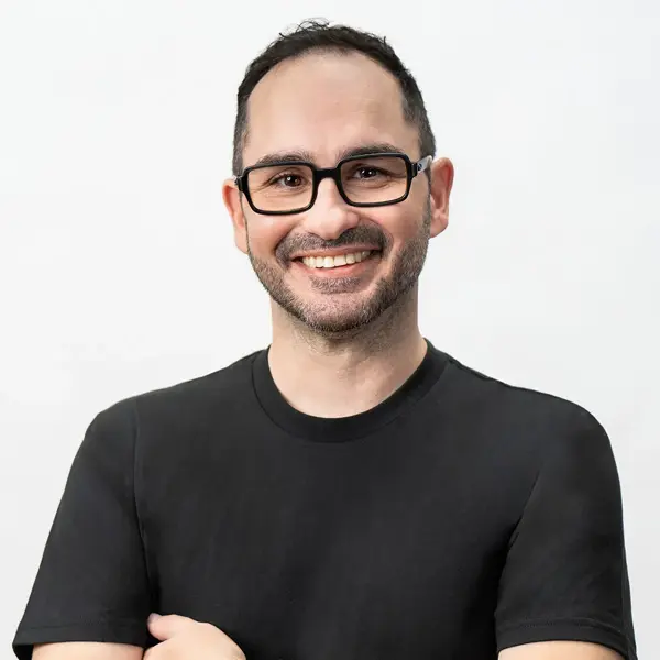Riccardo Kovacs, Post Supervisor, with short dark hair, glasses, and a beard, smiles at the camera. He wears a plain black t-shirt and stands against a white background.