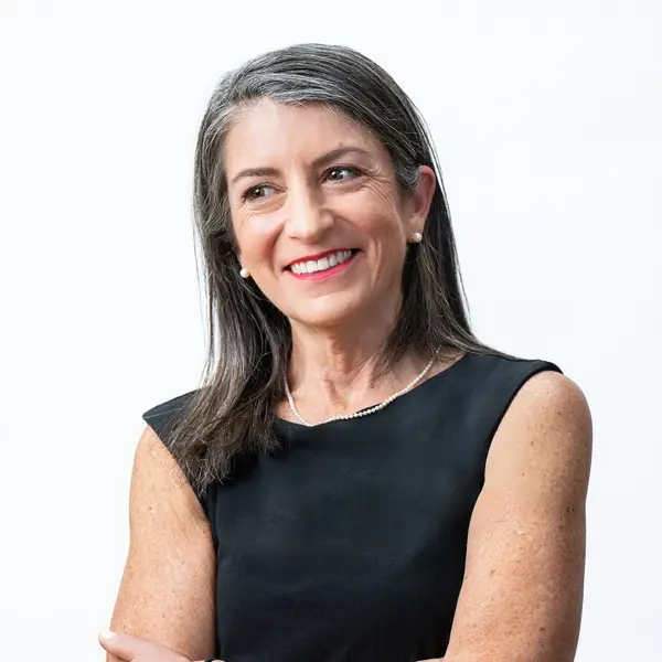 Sarah McDonald, Controller, a confident middle-aged woman with long gray hair, wearing a sleeveless black dress, pearl necklace, and pearl earrings, smiles while looking to the side against a plain white background.