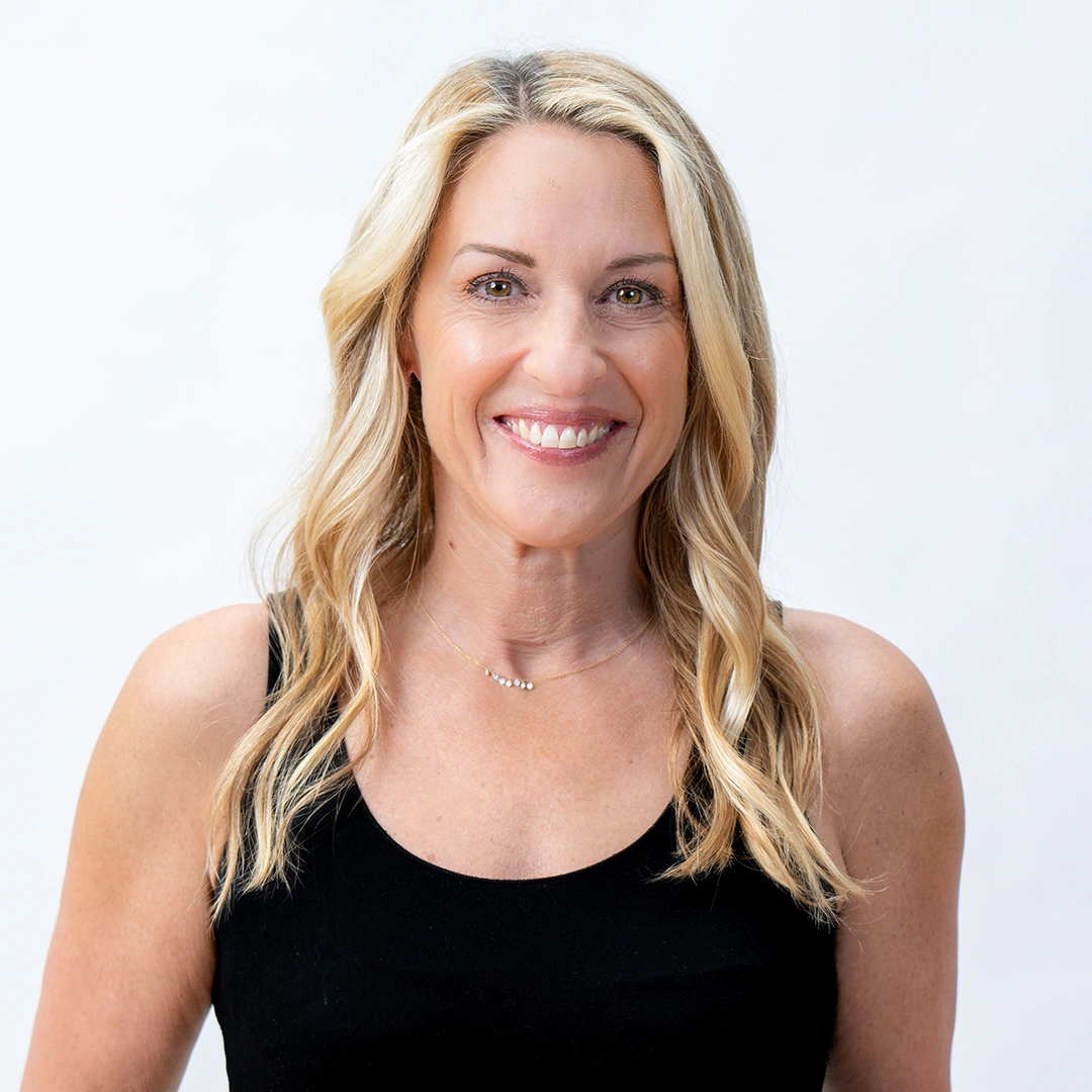 A smiling woman with long blonde hair, wearing a black sleeveless top, stands in front of a plain white background—an image of Jill Hackett, ACCOUNT DIRECTOR.
